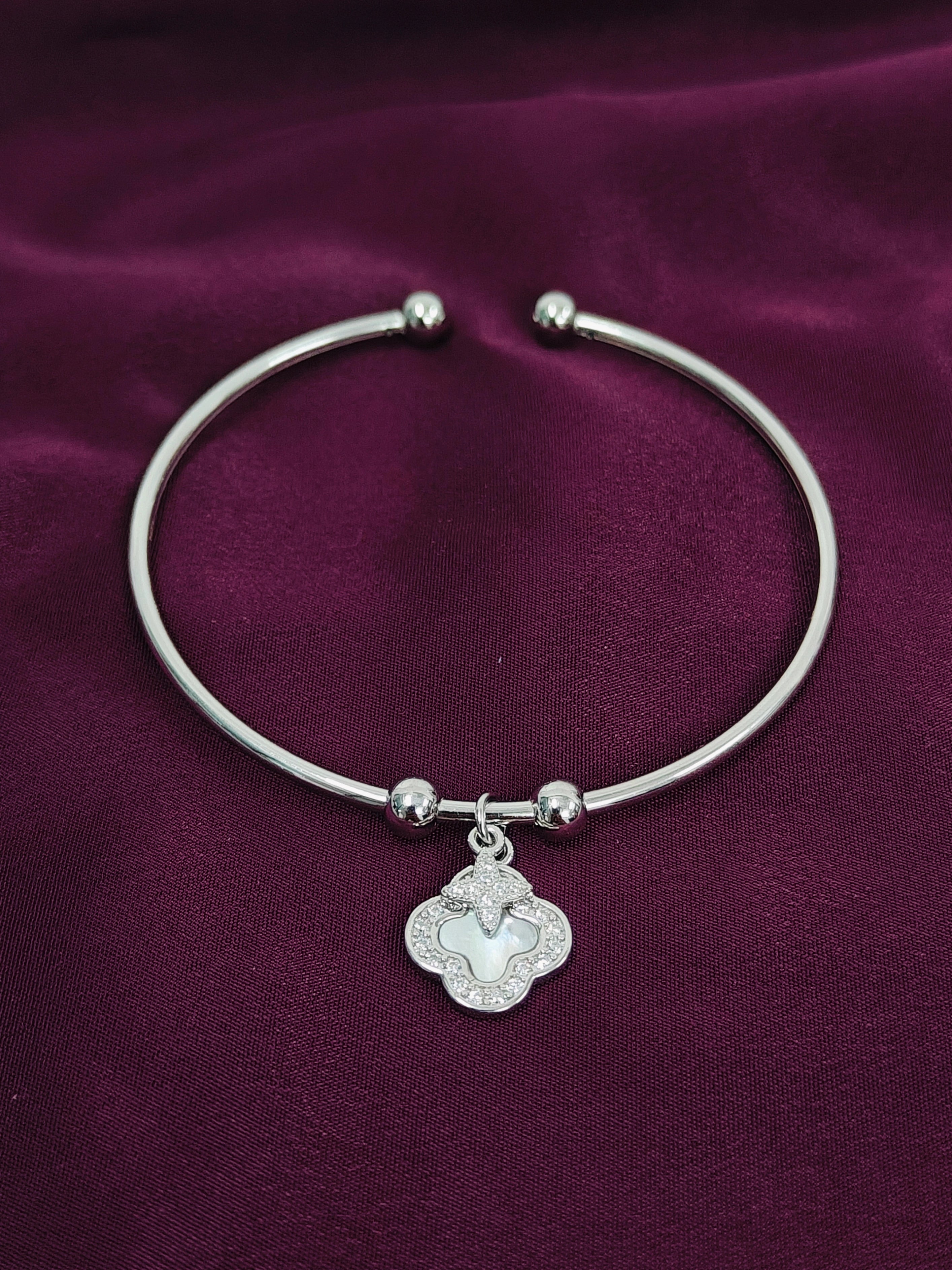 Silver bracelet with a clover-shaped charm on a purple fabric background